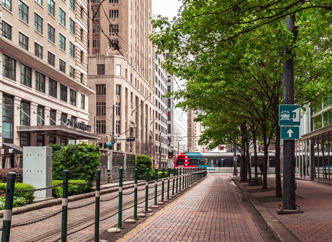 Houston, TX - Downtown Street Scene With A Light Rail Train Passing Beneath Shaded Trees Near A Hotel